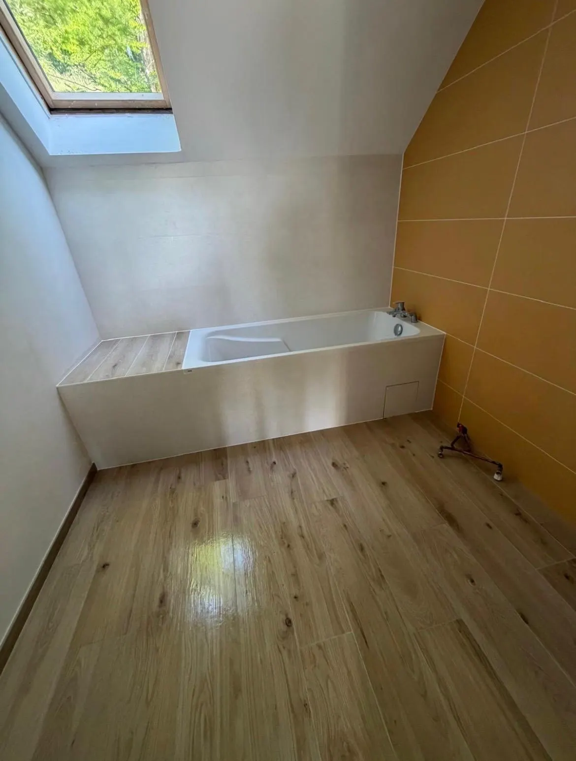 Salle de bains sous combles : sol imitation parquet, habillage de baignoire et mur en faïence ocre