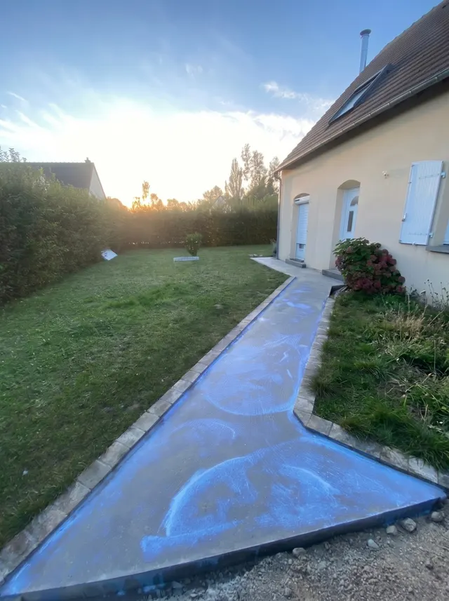 Allée enduite de primaire d'accroche bleu avant la pose, le long d'une pelouse