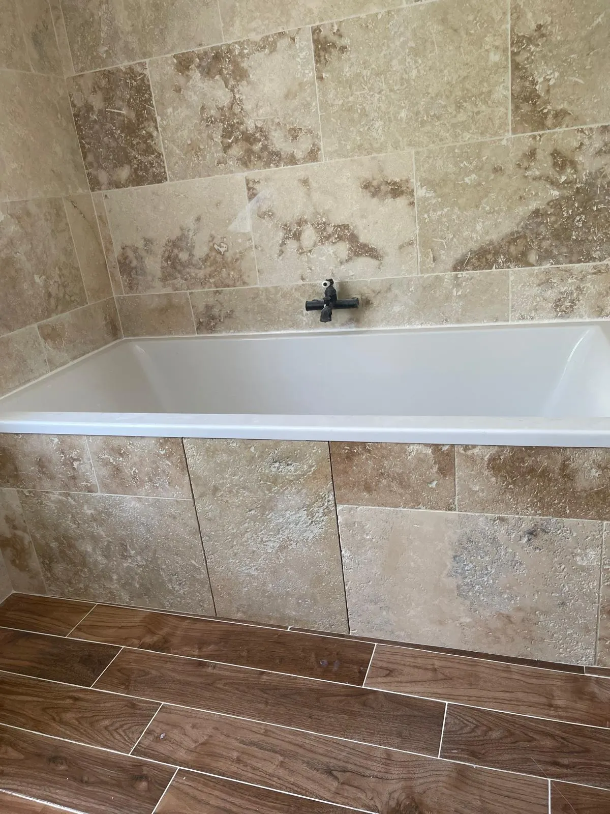 Baignoire encastrée, tablier et murs en travertin, sol en carrelage imitation bois foncé