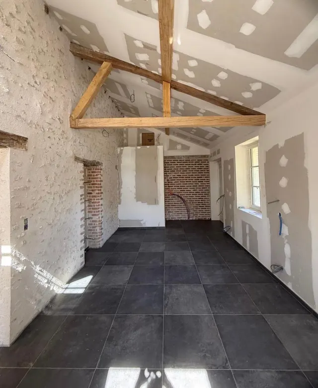 Pièce rénovée aux murs de pierre et de briques, sol en grands carreaux anthracite