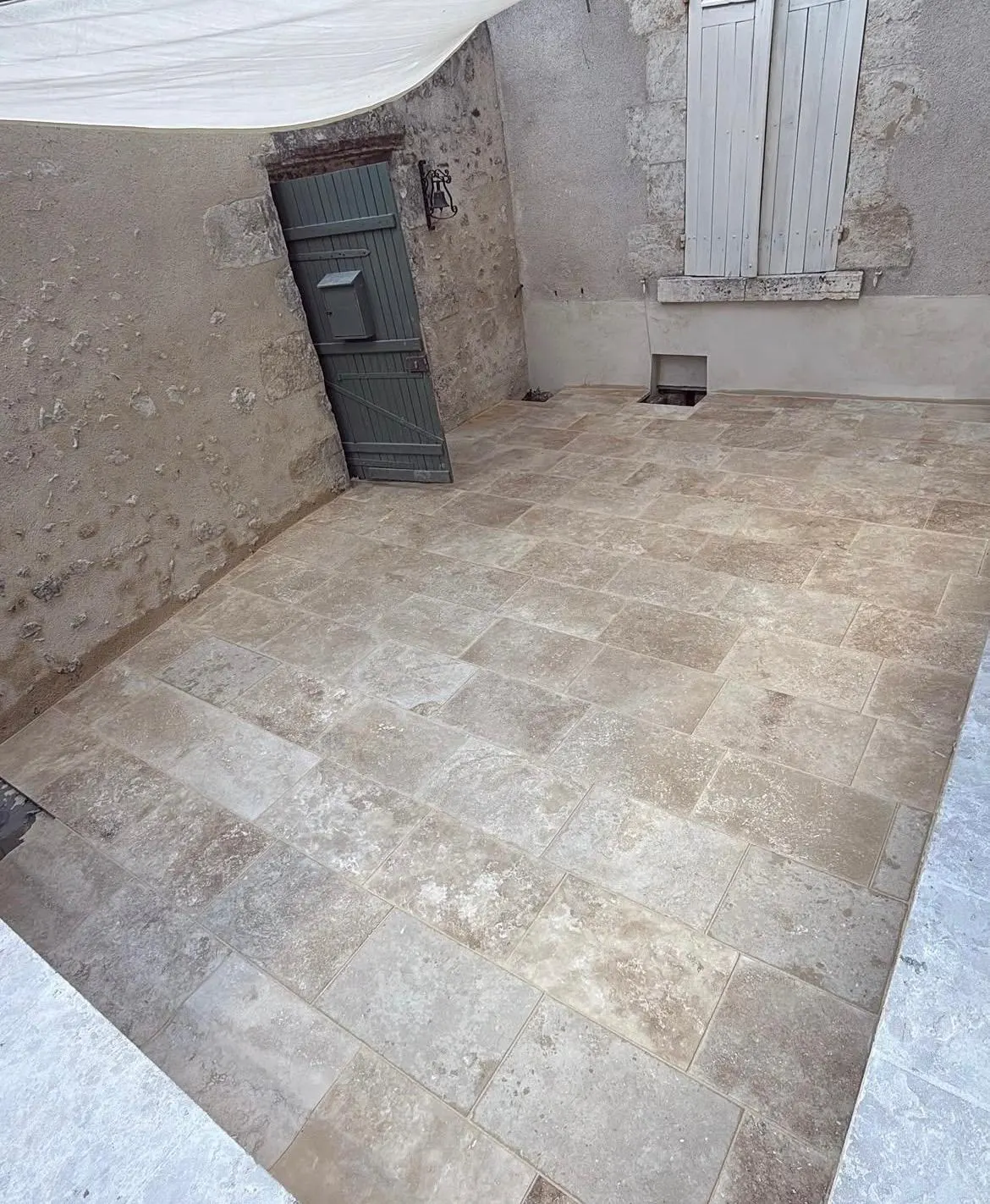 Cour intérieure dallée de travertin sous une voile d'ombrage, contre des murs en pierre